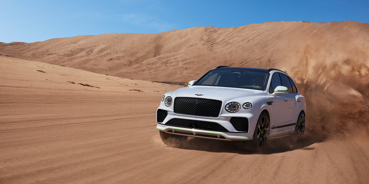 Bentley Muscat Bentley Bentayga Speed SUV front three quarter in Snow Quarts Pearlescent by Mulliner white paint driving dynamically through the desert