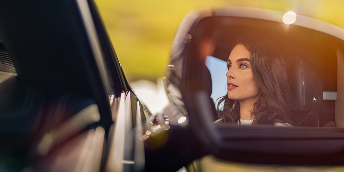 Bentley Muscat profile of dark haired woman's face in mirror of Bentley car in sunlight