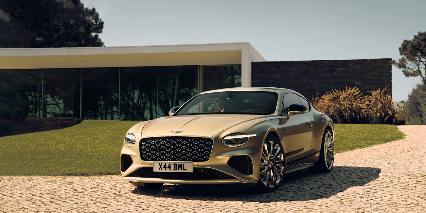 Bentley Muscat Bentley Continental GT Mulliner coupe front three quarters in Patina paint parked outside a glass fronted building with a grass lawn behind it