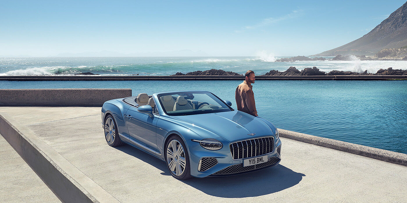 Bentley Muscat New Bentley Continental GTC Azure convertible front view in Light Windsor blue paint with 22 inch ten spoke wheels parked by the sea in the sunshine
