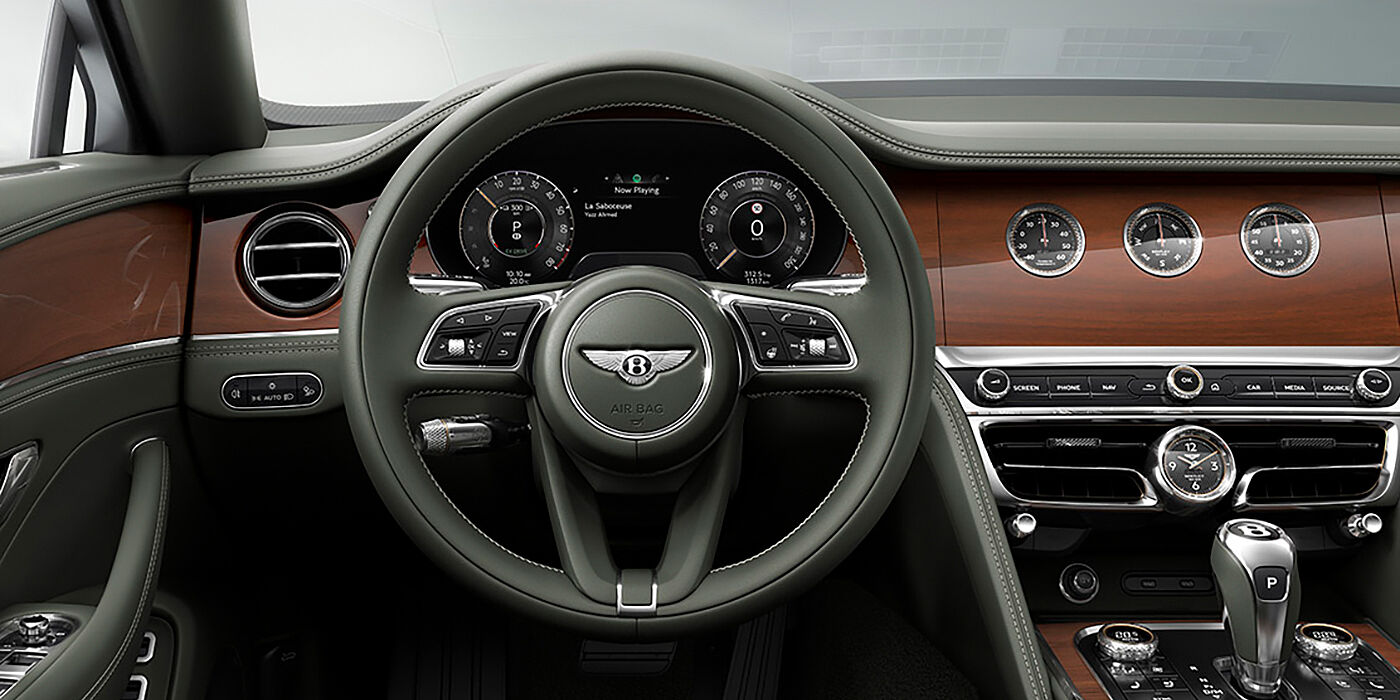 Bentley Muscat New Bentley Flying Spur sedan front cabin in Cumbrian Green hide and Crown Cut walnut veneer showing steering wheel and Rotating Display with three clocks on face