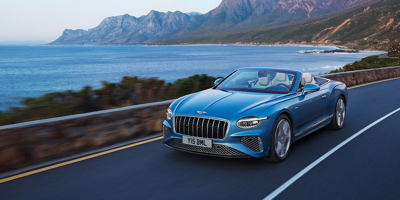 Bentley Muscat New Bentley Continental GTC Azure convertible in Light Windsor blue paint with 22 inch Azure wheels and chrome grill, driving dynamically by the sea