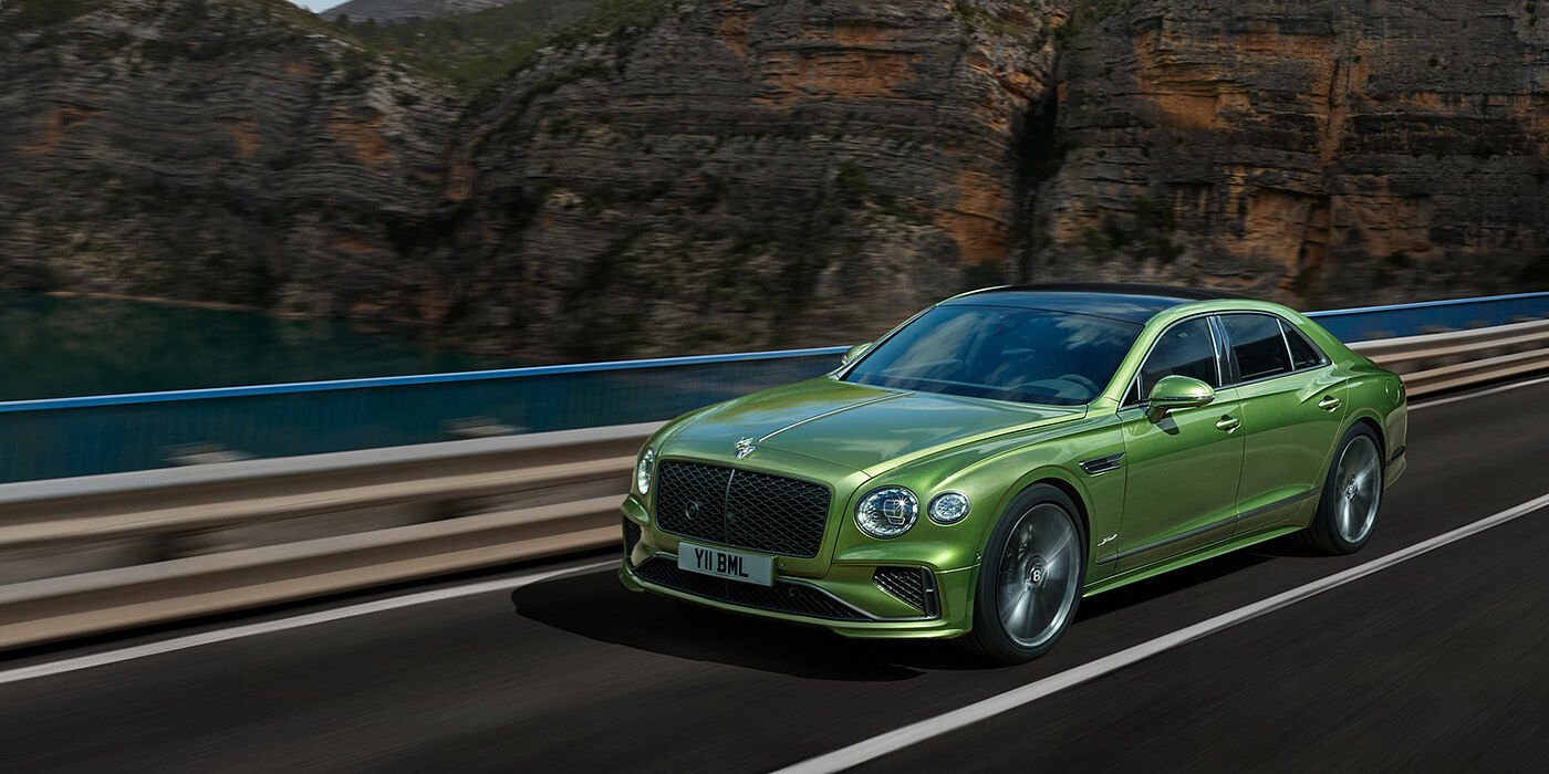 Bentley Muscat Bentley New Flying Spur Speed v8 hybrid sedan driving dynamically on a mountain road in Tourmaline Green paint