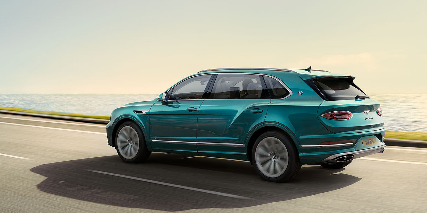 Bentley Muscat Bentley Bentayga Extended Wheelbase Azure luxury SUV rear three quarter in Topaz Blue by Mulliner paint, driving on an ocean road.