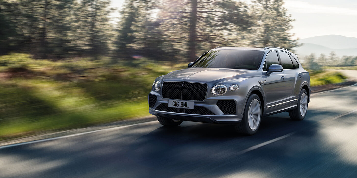 Bentley Muscat Bentley Bentayga luxury SUV front three quarter in Moonbeam paint, driving on an country road past trees.