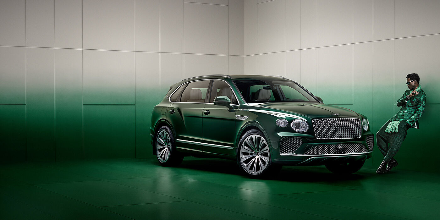 Bentley Muscat Wisdom K leans against wall next to Bentley Bentayga Extended Wheelbase Atelier Edition SUV in Light Emerald green paint