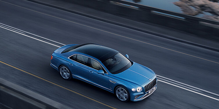 Bentley Muscat New Bentley Flying Spur Azure sedan in Light windsor blue paint by Mulliner, with 22 inch Azure wheels seen from overhead driving dynamically on a country road