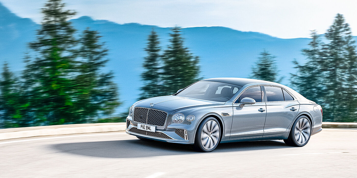 Bentley Muscat New Bentley Flying Spur sedan side view in Silverlake paint with ten spoke wheels and chrome matrix grille driving dynamically on a mountain road