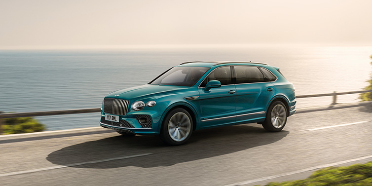 Bentley Muscat Bentley Bentayga Extended Wheelbase Azure SUV in Topaz blue paint driving dynamically by the ocean