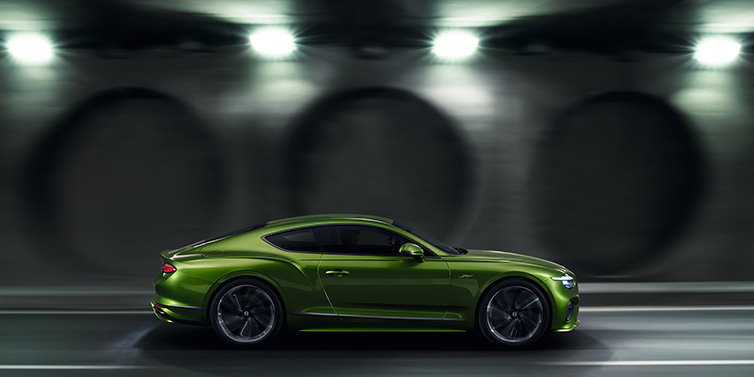 Bentley Muscat Bentley Continental GT Speed coupe profile in Tourmaline Green driving dynamically past a concrete wall at night