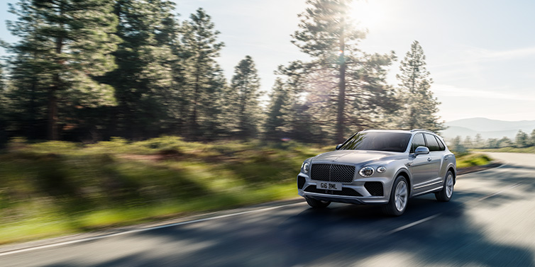 Bentley Muscat Bentley Bentayga SUV front three quarter in Moonbeam silver paint driving dynamically along a tree-lined road