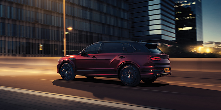 Bentley Muscat Bentley Bentayga Extended Wheelbase Mulliner SUV in Cricket Ball red paint driving dynamically in city at night