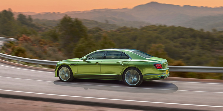 Bentley Muscat Bentley Flying Spur Speed sedan side profile in Tourmaline Green paint driving dynamically on a mountain road at sunset