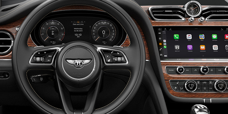 Bentley Muscat Bentley Bentayga SUV front interior detail of steering wheel and driver screens surrounded by Beluga black hide and Crown Cut Walnut veneer